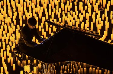 An artist playing piano surrounded by lit candles at a Candlelight event.