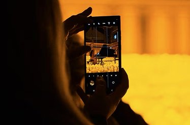 A person taking a picture of a grand piano surrounded with candles.