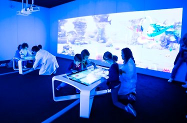 Children interact with digital tables at Chaos Lab, projecting their drawings onto a large immersive wall.