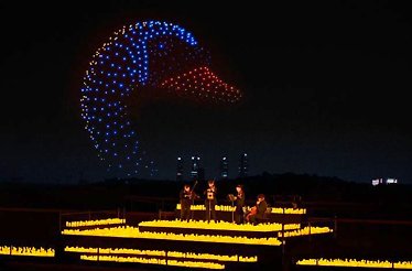 A string quartet performing at a candlelit outdoor DroneArt Show, while 1,000 drones form a giant glowing swan in the night sky.