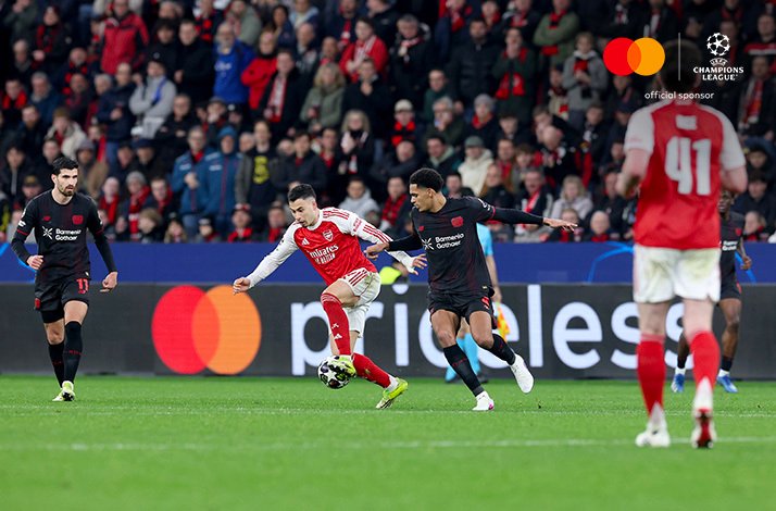 An Arsenal attacker controls the ball under pressure from a Bayer Leverkusen player in the UEFA Champions League.