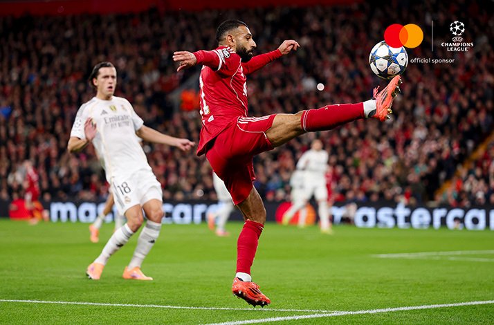 Liverpool player controls a high ball as a Real Madrid player watches during UEFA Champions League.