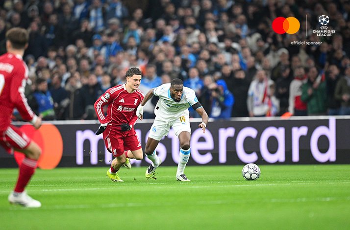 Marseille attacker sprints onto a loose ball as Liverpool defender chases during UEFA Champions League game.