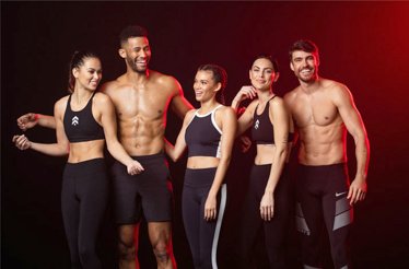 Three female and two male fitness models are posing at a dimly-lit black-and-red background.