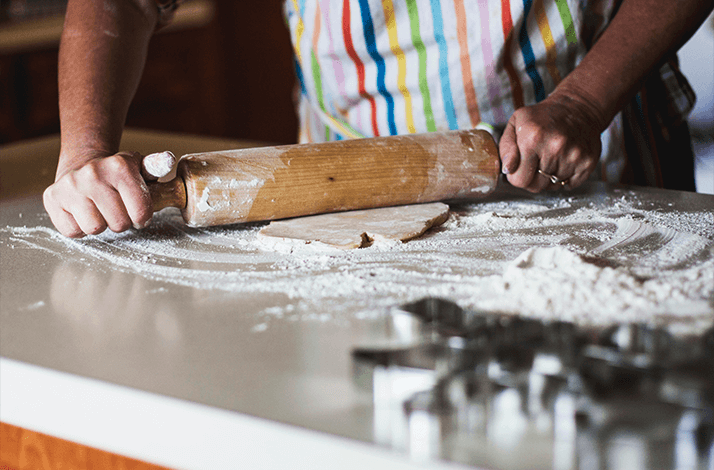 Person using a rolling pin to flatten dough dusted with flour on a kitchen counter.