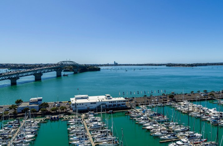 Bright daytime view of Westhaven Marina, Auckland Harbour Bridge, and turquoise waters with docked boats