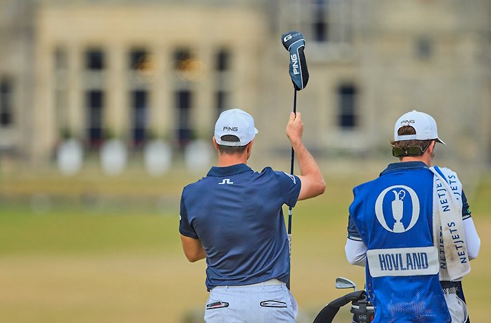 Viktor Hovland raising a Ping club while his caddie stands alongside, with the Royal & Ancient clubhouse at St Andrews behind them.