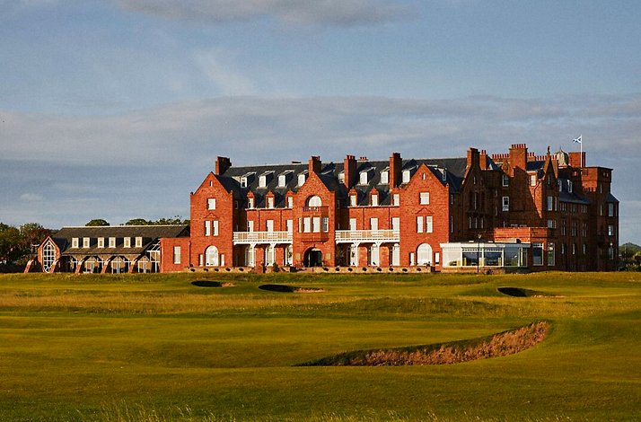 Large red-brick building with multiple chimneys overlooking a green golf course.