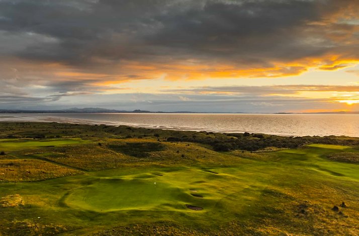 Sunset over a coastal golf course with rolling green fairways and a calm sea.