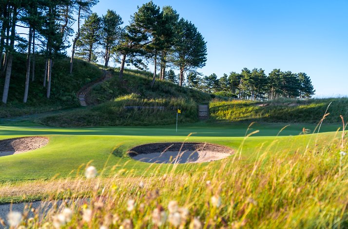 Royal Birkdale Golf Club green and bunkers with flag, surrounded by dunes and pine trees.