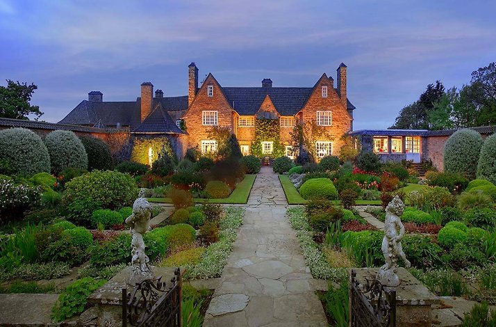 Historic stone manor with warm lights, surrounded by a lush, symmetrical garden
