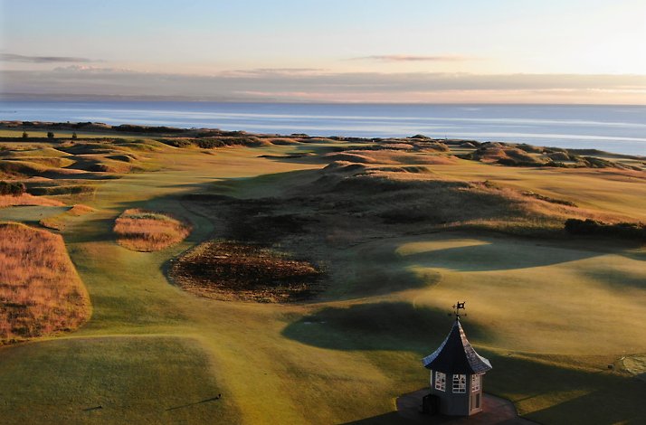 The Kingsbarns Golf Links course featuring a small stone starter hut overlooking coastal dunes and the sea in Scotland.