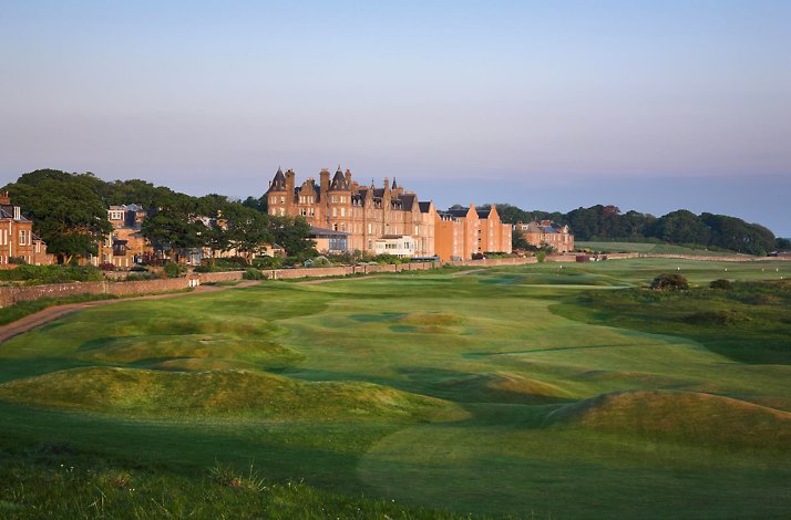 Historic stone building overlooking a wide, green golf course under a clear sky.