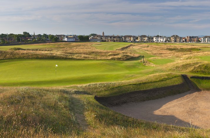Golf course with a sand bunker and town in the background.