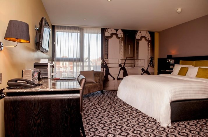 Vincent Hotel Southport modern guest room with bed, desk, and large window.