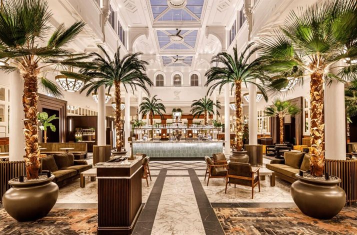 Opulent hotel lobby with a large bar and tropical palm trees.