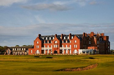 Large red-brick building with multiple chimneys overlooking a green golf course.