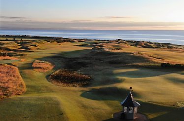 The Kingsbarns Golf Links course featuring a small stone starter hut overlooking coastal dunes and the sea in Scotland.
