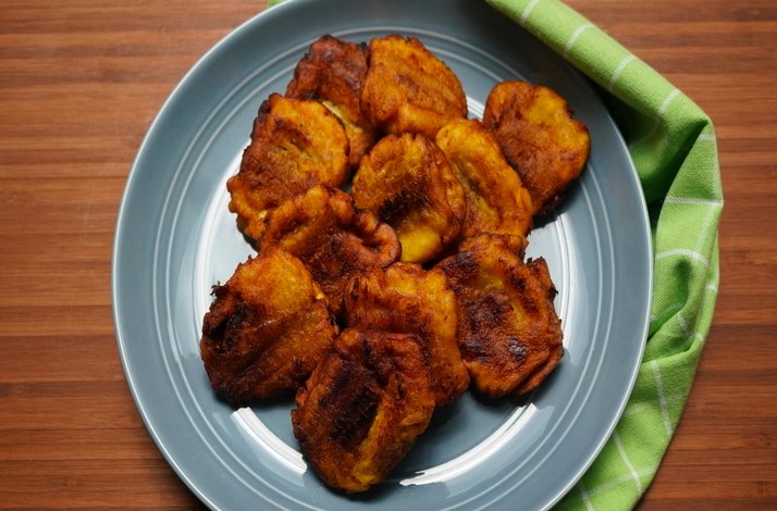 Golden fried plantains arranged on a blue plate, served on a wooden table with a green napkin.