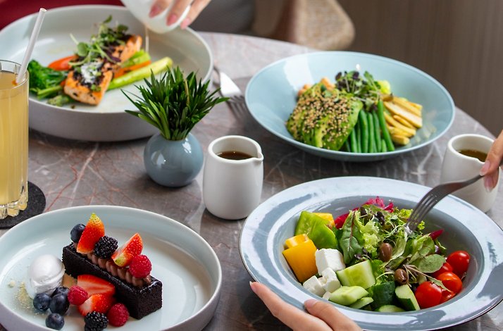 Table with salad, salmon dishes, dessert with berries, and drinks at Four Seasons Hotel Singapore.
