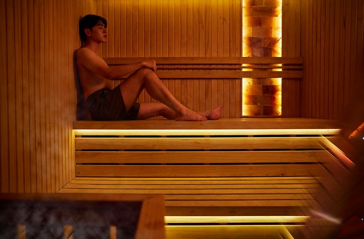 Guest relaxing on a wooden bench in a warmly lit sauna at Four Seasons Hotel Singapore spa.