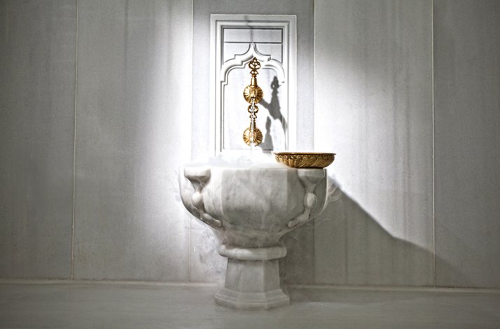 A traditional marble fountain inside Hürrem Sultan Hammam with steam rising around it.