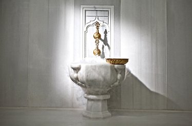 A traditional marble fountain inside Hürrem Sultan Hammam with steam rising around it.