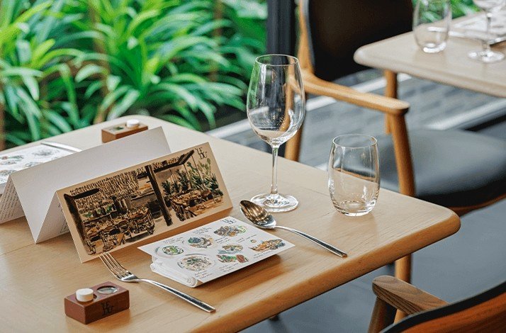 A table in Le Du is set for a meal with a folded menu, a fork, a spoon, and two empty glasses.
