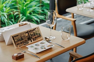 A table in Le Du is set for a meal with a folded menu, a fork, a spoon, and two empty glasses.