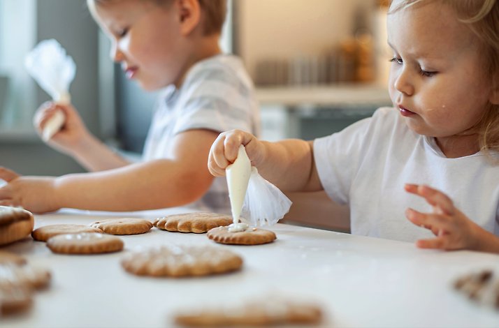 Children decorating cookies with icing on a table.