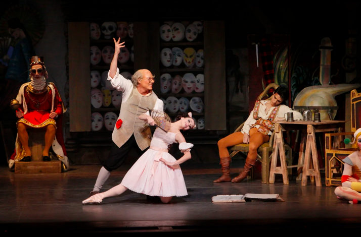 Ballet duet with dramatic pose; background features masks, a king, and a rustic tavern scene.