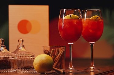 Two glasses of Mediterranean Sangria garnished with cinnamon with the Mastercard logo visible in the background.