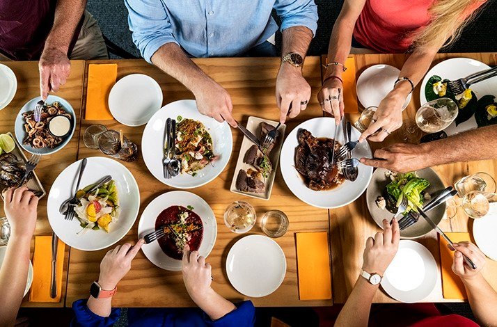 A dinner table captured from above with hands helping themselves.