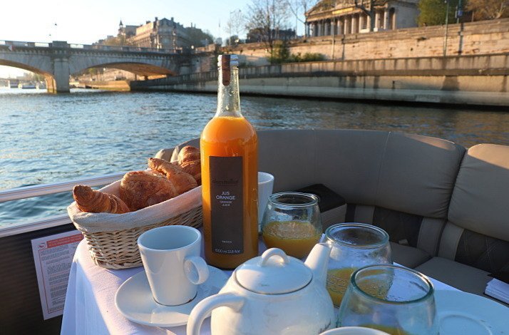 Breakfast on board of cruise boat that includes bottle of orange juice, teapot, cups and croissants.