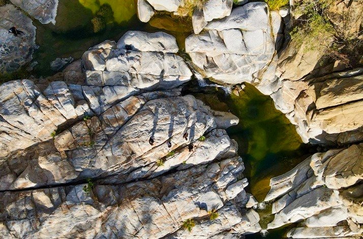 Aerial view of rocky formations and green pools at Cañón de la Zorra in Mexico's Sierra de la Laguna, with people visible on the rocks.
