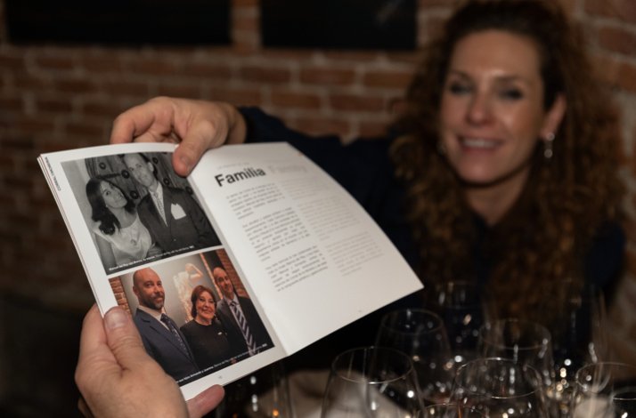 A lady happily presenting a small book with the history of Corral Moreira to another person.