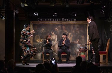 A lively flamenco performance at Corral de la Morería, with a vibrant dancer in motion and three musicians applauding enthusiastically onstage.