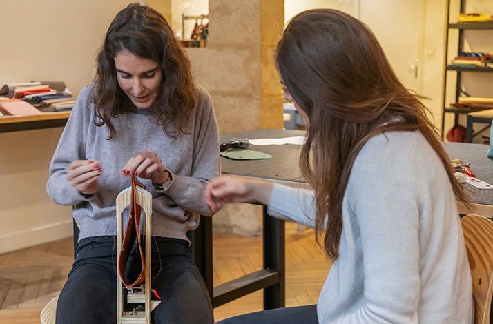 Two women in the process of making handbag during leatherworking masterclass at Atelier La Patine in Paris. 