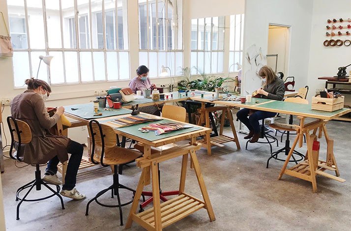Three women sitting at desks and crafting during leatherworking masterclass at the Atelier La Patine in Paris.