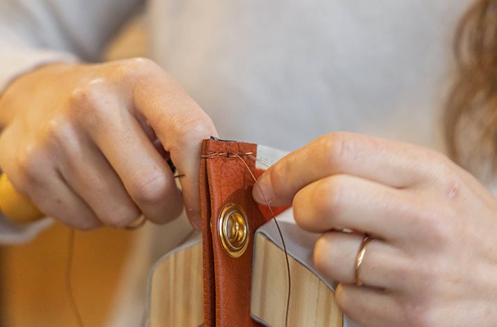 A close-up of woman’s hands in the process of stitching leather.