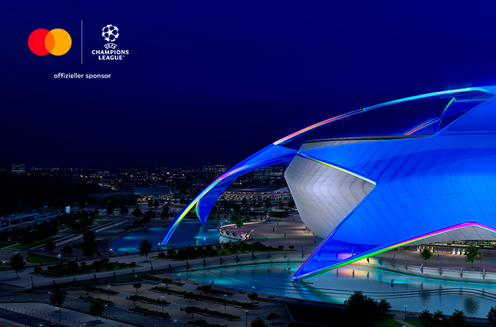 Fußball Arena München illuminated in blue at night with Mastercard 'offizieller sponsor' branding in upper-left corner.