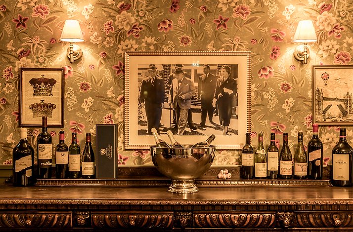 Little London Bar and Grille bar display featuring Pol Roger champagne bucket, wine bottles, vintage framed photo, and floral wallpaper.
