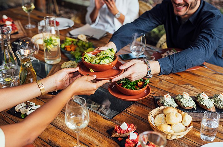 Person passing over a dish during dinner at EMIL restaurant in Dortmund. On the table there are various dishes, snacks and drinks.