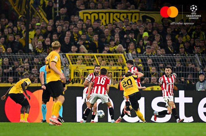 Dortmund and Athletic Club players contesting possession before a packed yellow crowd; Logos of Mastercard and UEFA Champions League in the upper-right corner.