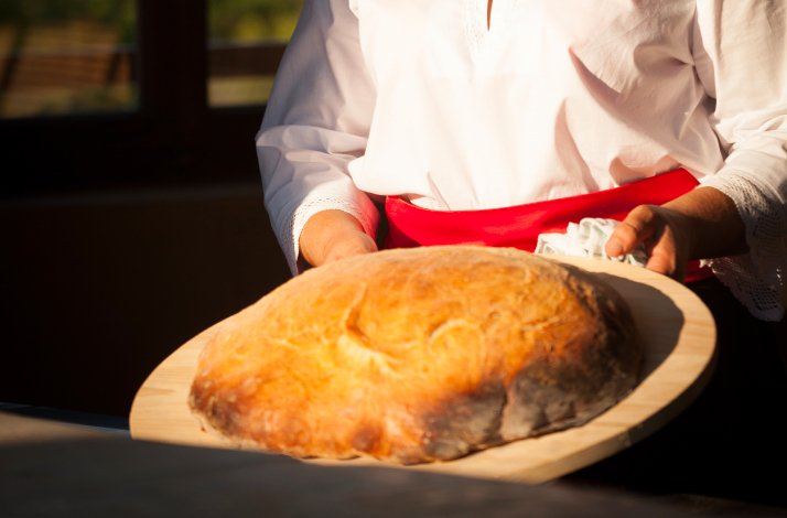 Cook holding a wooden board with homemade bread cooked during the workshop in Stella Croatica.