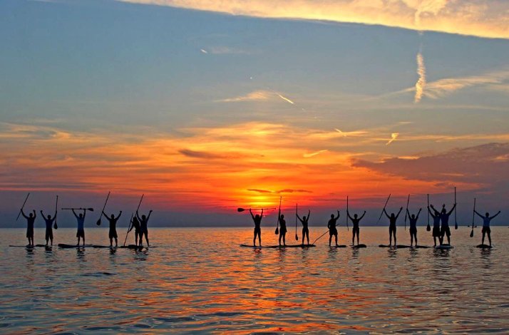 A group of people posing on SUP boards with sunset in the background