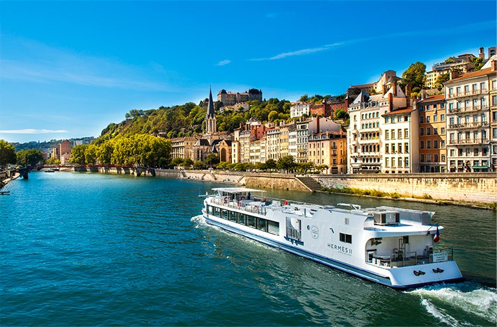 Soak up Lyon's picturesque landscapes on a dining cruise with Les Bateaux Lyonnais: In Lyon, France Houses on one of Lyon’s riverbanks with a cruise boat passing along.