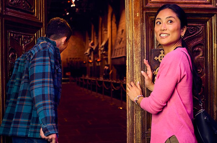 An excited visitor peers through the grand ornate wooden doors of the Hogwarts Great Hall set at the Warner Bros. Studio Tour London – The Making of Harry Potter.