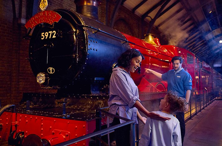 A mother and child share a magical moment beside the iconic scarlet Hogwarts Express steam engine (5972) at Platform 9¾, assisted by a Studio Tour guide at Warner Bros. Studio Tour London.
