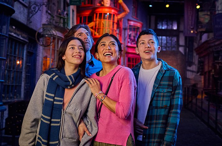 A delighted family of four gazes in wonder at the elaborate recreation of Diagon Alley™, surrounded by the colourful wizarding world shopfronts at Warner Bros. Studio Tour London – The Making of Harry Potter.